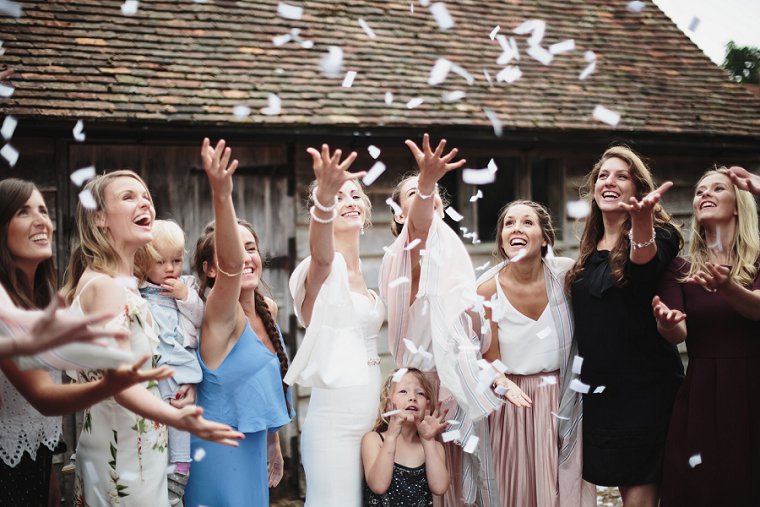 Bride and friends throwing confetti in the air at her wedding at Ratsbury Barn