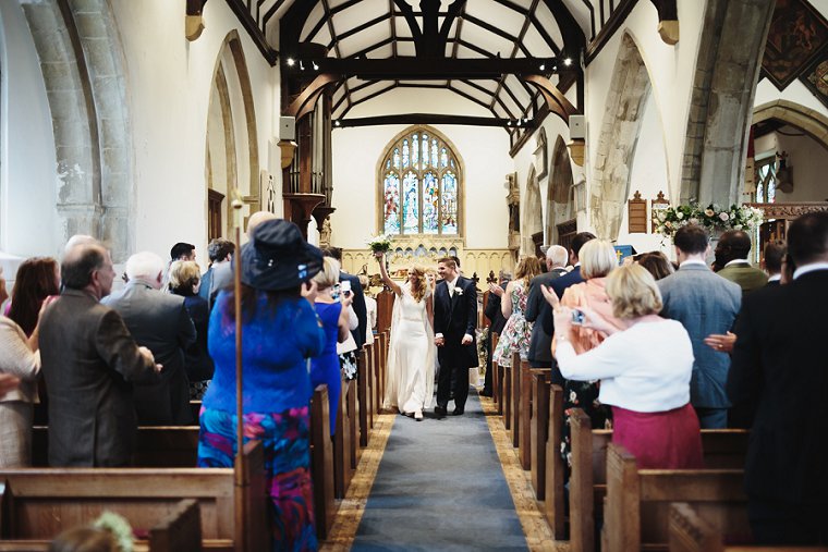 Bride holding her bouquet in the air as she leaves the church