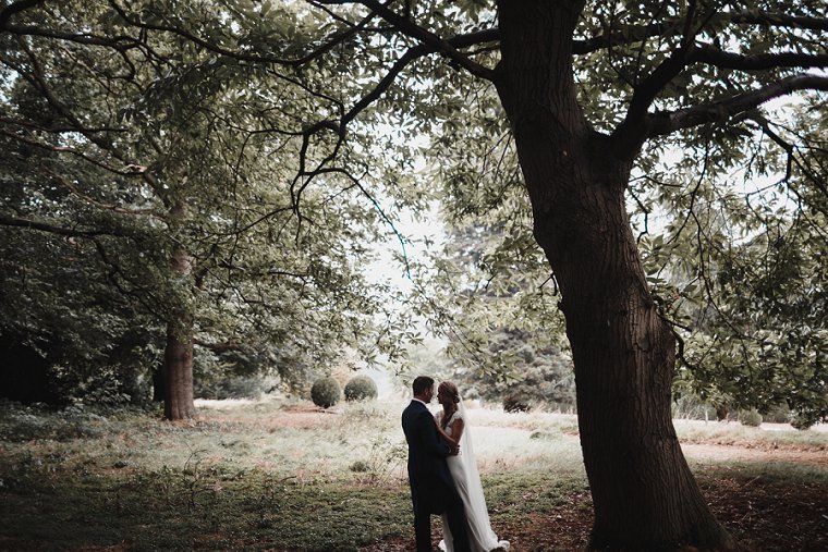 Wedding photography during rain storm at Squerryes Court as Bride and Groom take cover under tree