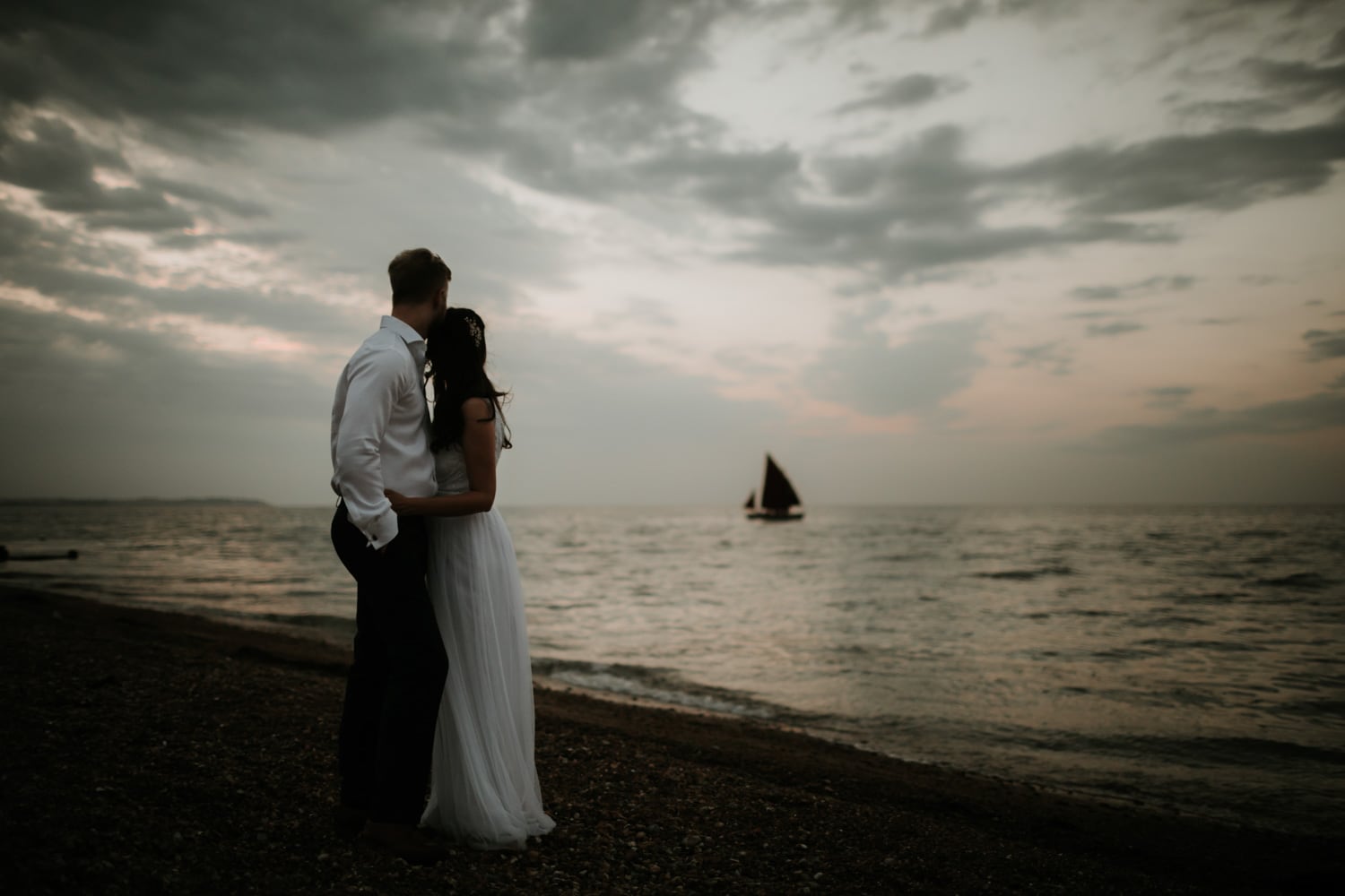 Bride and Groom on Whitstable beach with a sail boat in the distance at sea
