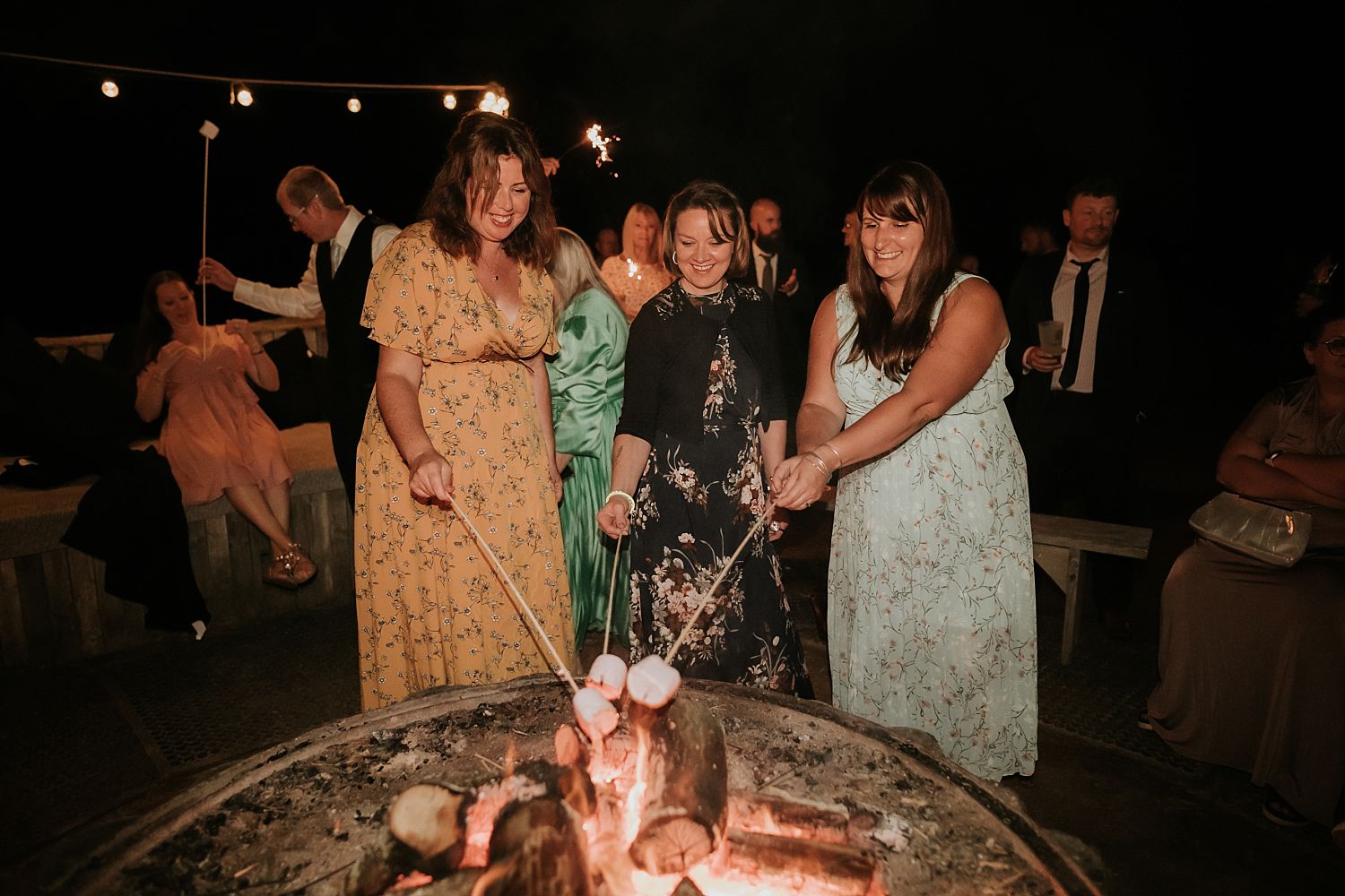 Wedding guests roasting marshmallows over a fire pit at The Dreys