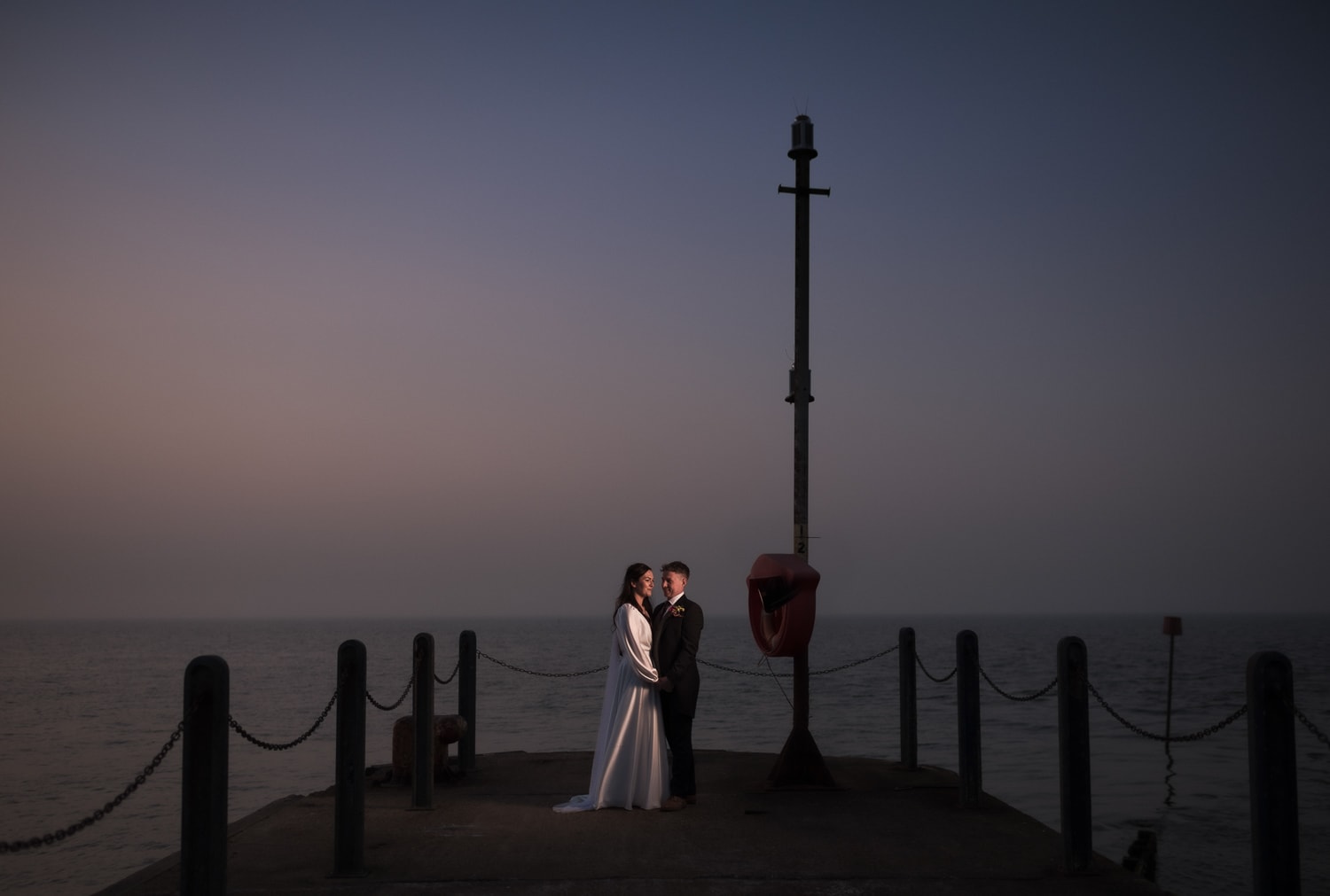 Bride and Groom posing for a photo at dusk next to the sea