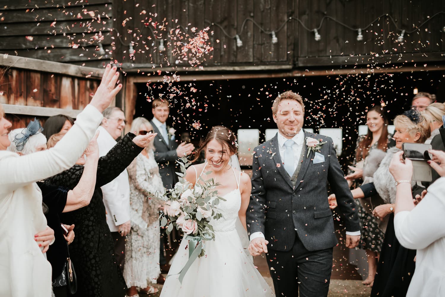 Bride and groom with guests throwing confetti at the great barn rolvenden