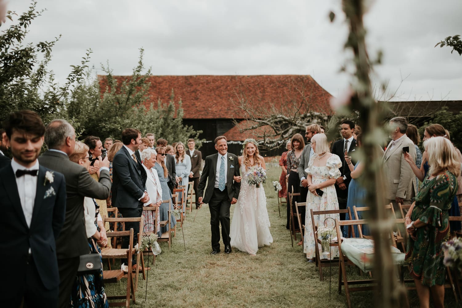 Bride and her father walking down the aisle in the orchard at The Great Barn in Rolvenden